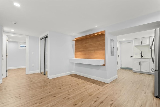 unfurnished living room featuring recessed lighting, baseboards, light wood-style floors, and a sink