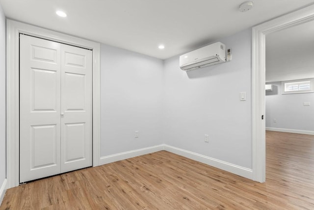 below grade area with light wood finished floors, recessed lighting, a wall mounted air conditioner, and baseboards