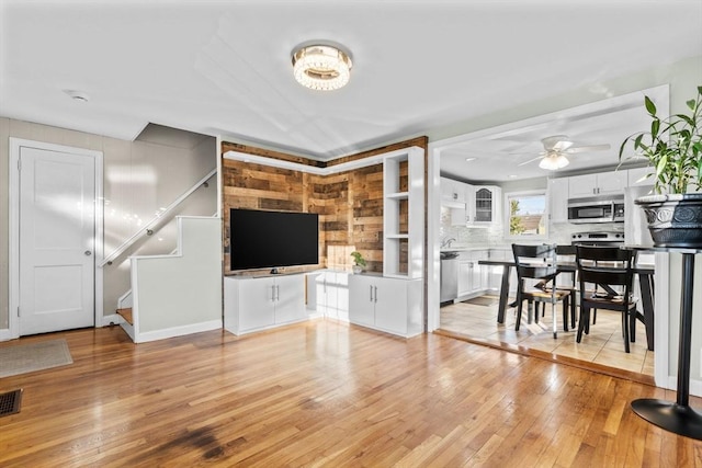 unfurnished living room with stairs, light wood-style flooring, ceiling fan with notable chandelier, and visible vents