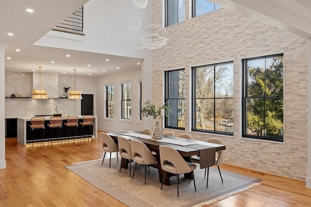 dining room with an inviting chandelier, light wood-style flooring, recessed lighting, and a towering ceiling