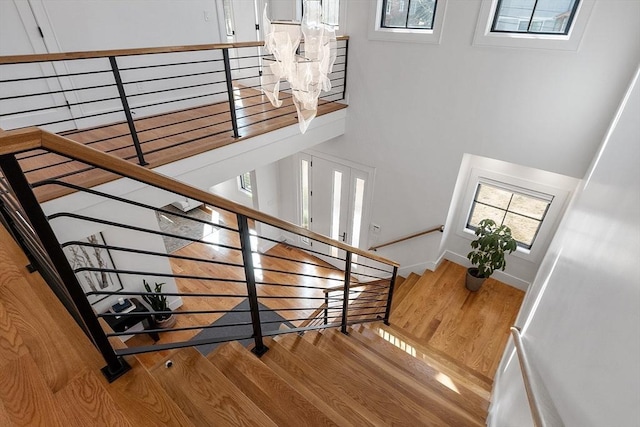 stairs with a wealth of natural light, wood finished floors, baseboards, and a towering ceiling