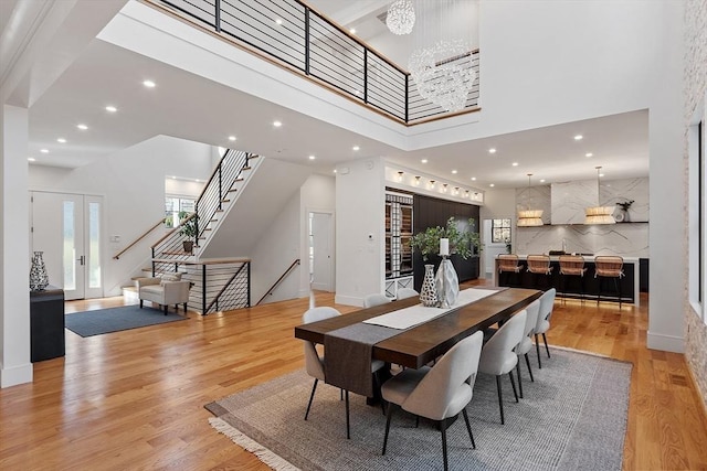 dining room featuring a wealth of natural light, light wood-style floors, a towering ceiling, and stairs