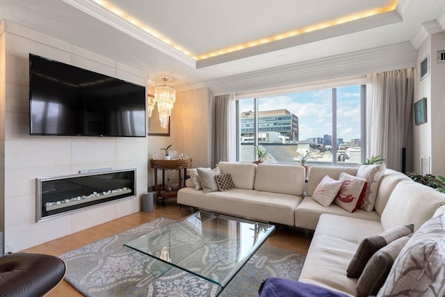 living room featuring a raised ceiling, a tiled fireplace, hardwood / wood-style flooring, and ornamental molding