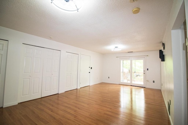 369 Aiken Ave Unit 15, Lowell, MA 01850 - unfurnished bedroom featuring a textured ceiling, light wood-style flooring, two closets, access to exterior, and baseboards