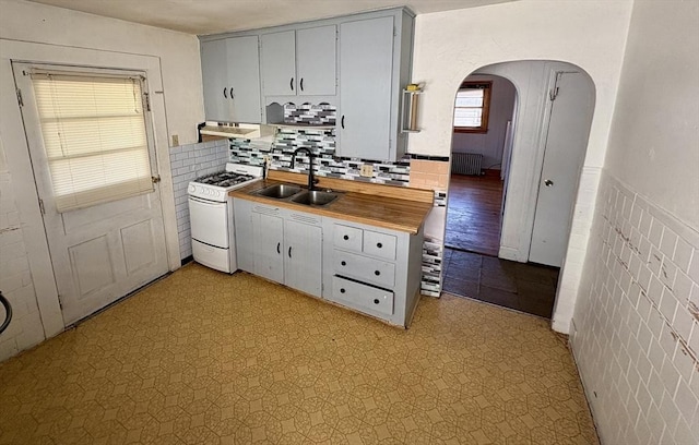 kitchen with radiator heating unit, sink, white range with gas stovetop, and tile walls