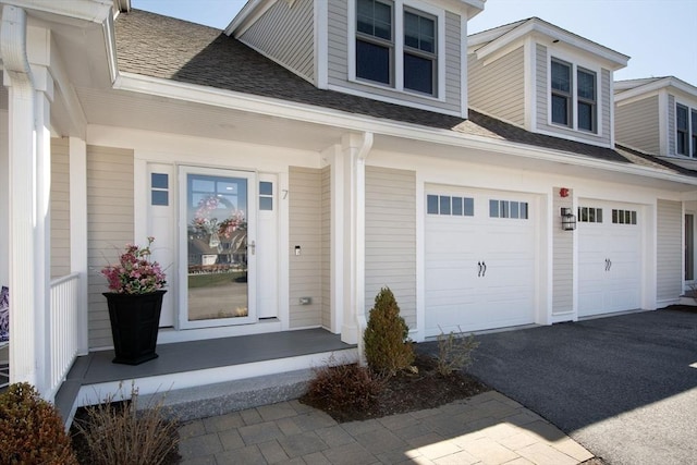 entrance to property featuring an attached garage, driveway, a porch, and a shingled roof