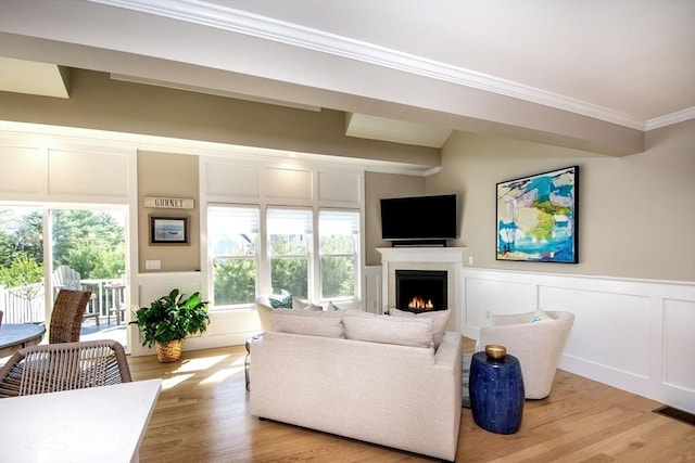 living area featuring a wainscoted wall, light wood-type flooring, a warm lit fireplace, crown molding, and a decorative wall