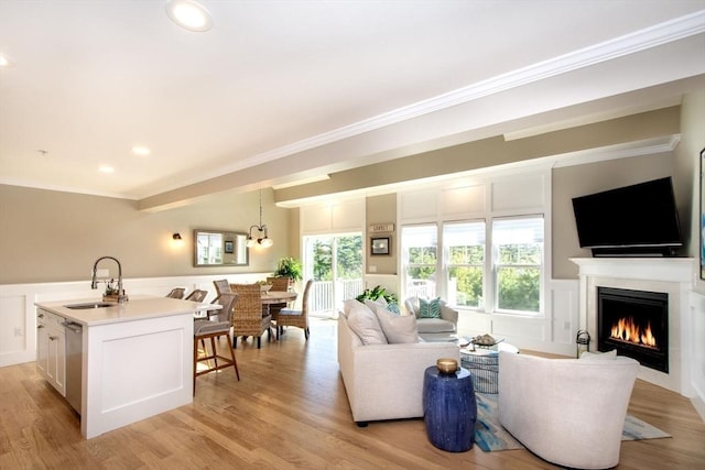 living room with a wainscoted wall, light wood-style floors, a lit fireplace, and crown molding