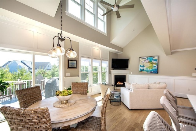 dining room with a high ceiling, light wood finished floors, a ceiling fan, a decorative wall, and a lit fireplace