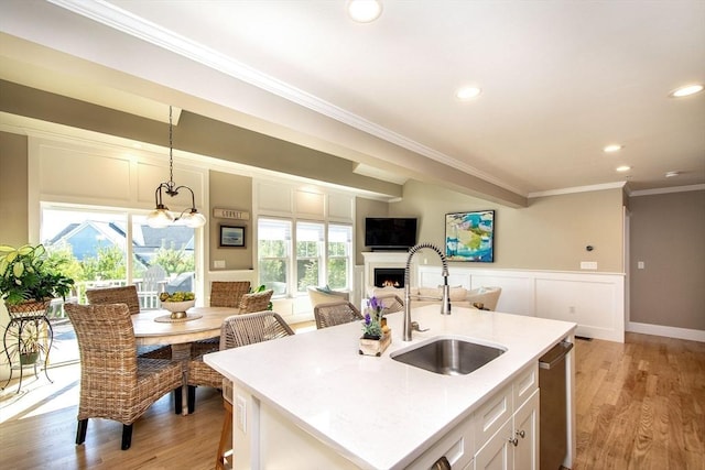 kitchen featuring a warm lit fireplace, crown molding, a sink, and light wood-type flooring