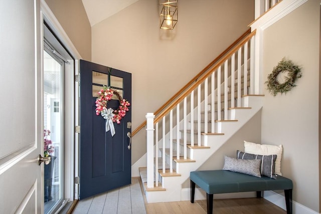 entryway with lofted ceiling, baseboards, wood finished floors, and stairway