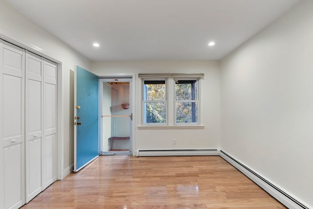 unfurnished bedroom with light hardwood / wood-style flooring, a closet, and a baseboard heating unit