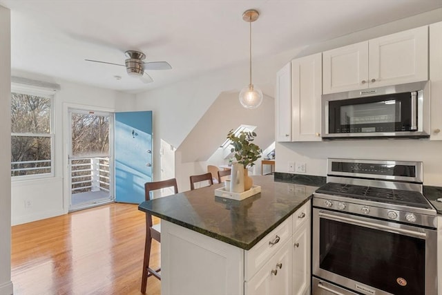 kitchen with appliances with stainless steel finishes, a kitchen breakfast bar, decorative light fixtures, light hardwood / wood-style flooring, and white cabinetry