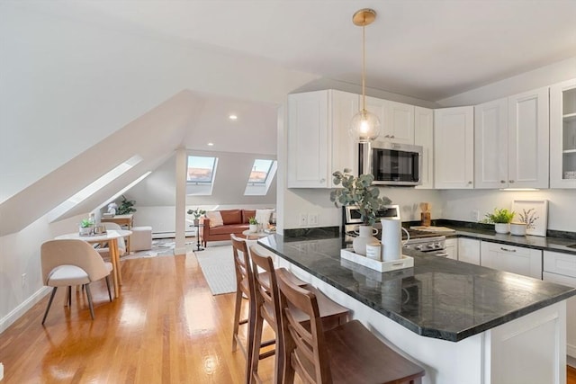 kitchen with a kitchen bar, kitchen peninsula, stainless steel appliances, pendant lighting, and white cabinetry