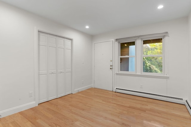 unfurnished bedroom featuring a baseboard radiator, light hardwood / wood-style flooring, and a closet