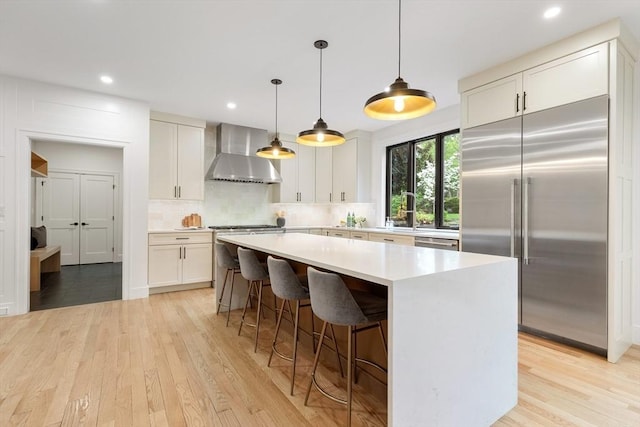 92 Cedar St, Lexington, MA 02421 - kitchen with wall chimney range hood, stainless steel appliances, a center island, light wood-style flooring, and recessed lighting