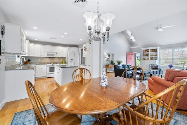 dining room featuring sink, ceiling fan with notable chandelier, light wood-type flooring, and lofted ceiling