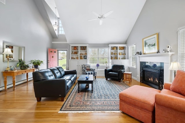 living room with a premium fireplace, light hardwood / wood-style flooring, a baseboard heating unit, ceiling fan, and high vaulted ceiling