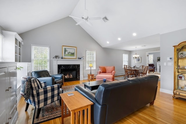 living room featuring a premium fireplace, high vaulted ceiling, light wood-type flooring, and ceiling fan with notable chandelier