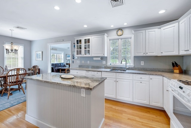 kitchen with light hardwood / wood-style floors, white appliances, hanging light fixtures, sink, and white cabinetry