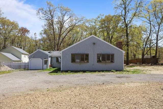 exterior space featuring an attached garage, dirt driveway, fence, and a chimney