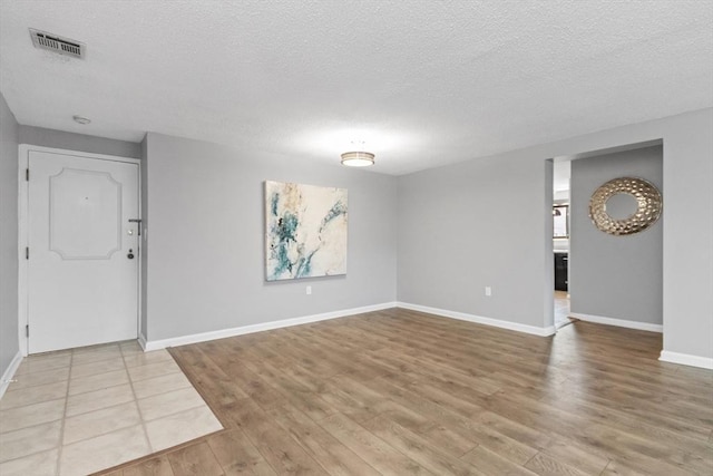 interior space with baseboards, light wood-style flooring, a textured ceiling, and visible vents