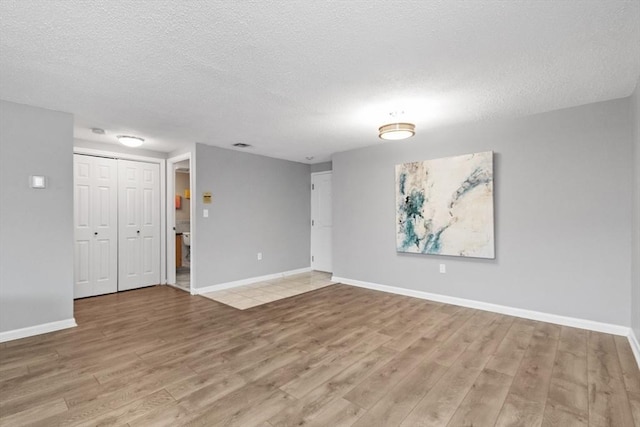 empty room featuring baseboards, a textured ceiling, and light wood finished floors