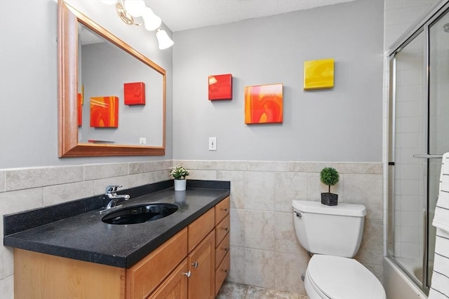 full bath with wainscoting, a shower with shower door, vanity, toilet, and tile walls