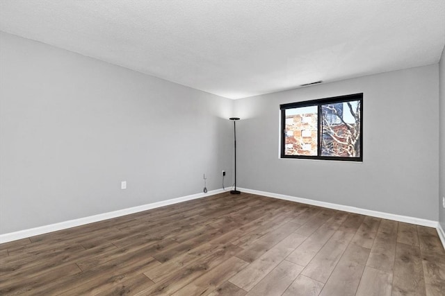 spare room featuring a textured ceiling, baseboards, visible vents, and dark wood-style floors