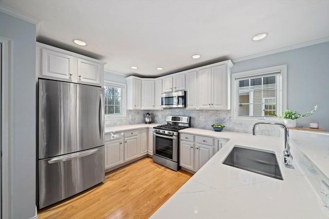 kitchen with sink, white cabinetry, crown molding, light stone counters, and appliances with stainless steel finishes