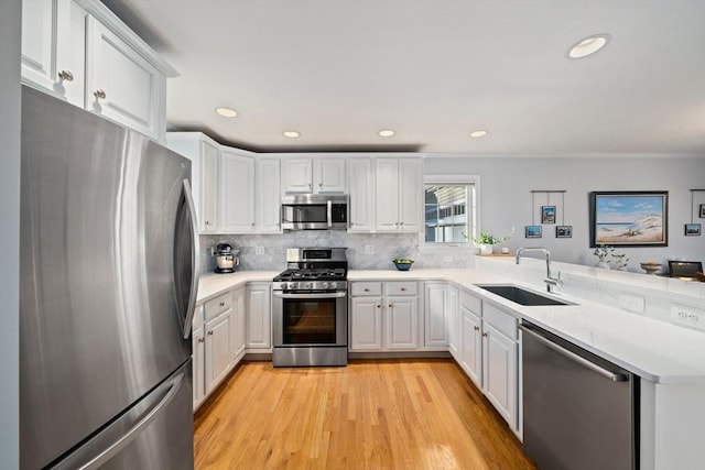 kitchen with white cabinetry, sink, decorative backsplash, stainless steel appliances, and light wood-type flooring