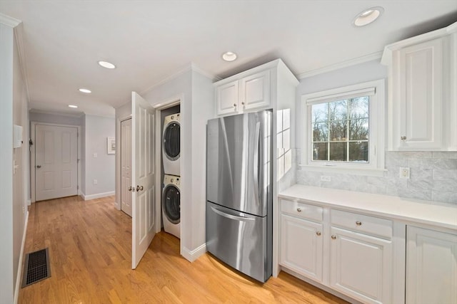 kitchen with white cabinetry, stacked washer and clothes dryer, stainless steel fridge, and crown molding