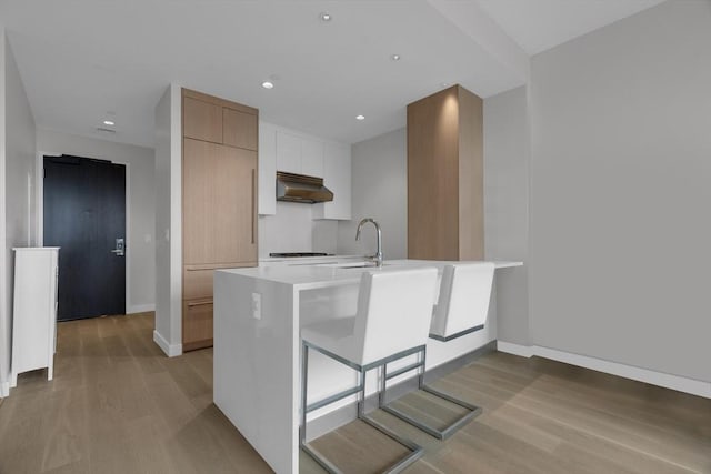 kitchen with sink, light wood-type flooring, white cabinetry, kitchen peninsula, and a breakfast bar area