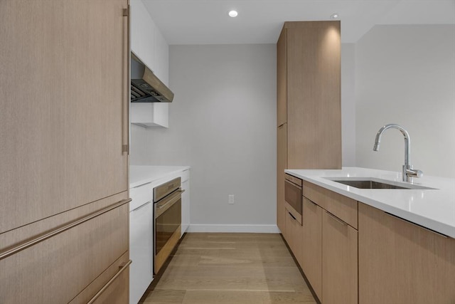 kitchen with light wood-type flooring, built in microwave, sink, oven, and range hood