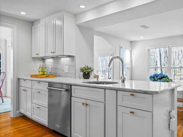 kitchen with light stone countertops, light wood-type flooring, a peninsula, dishwasher, and a sink