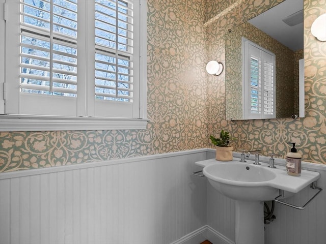bathroom with a wealth of natural light, wallpapered walls, and a wainscoted wall