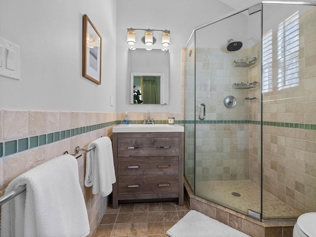 bathroom featuring a stall shower, vanity, wainscoting, and tile walls
