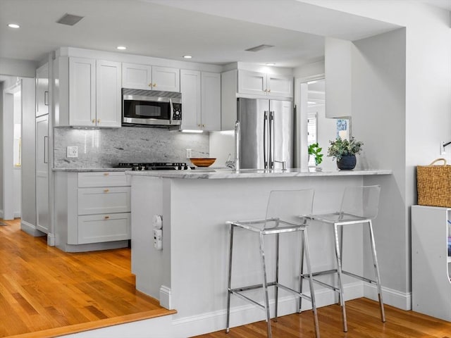 kitchen featuring light wood-style floors, decorative backsplash, a kitchen breakfast bar, and stainless steel appliances