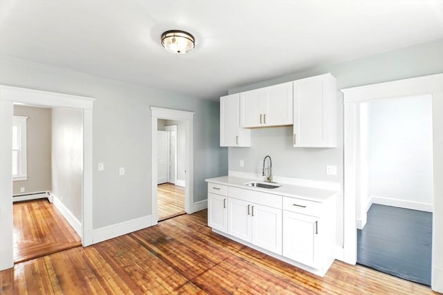 kitchen with a sink, white cabinetry, baseboards, light countertops, and a baseboard radiator