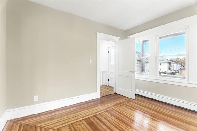 unfurnished room featuring wood finished floors, baseboards, and a baseboard heating unit