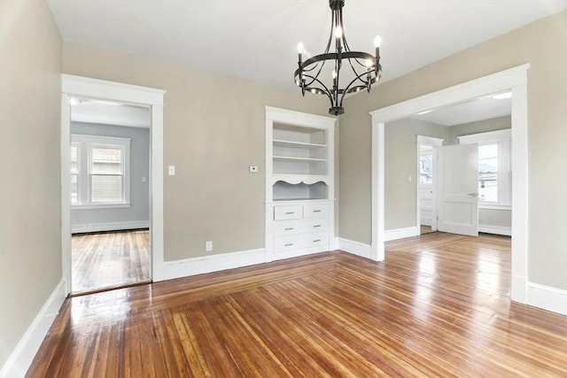 unfurnished dining area with an inviting chandelier, baseboards, plenty of natural light, and wood finished floors