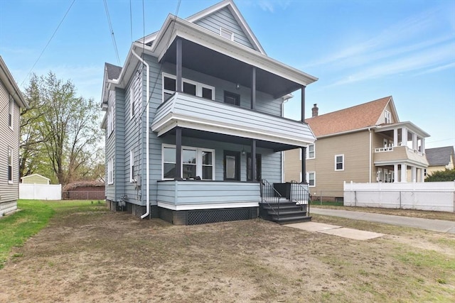 rear view of house with a balcony, a porch, and fence