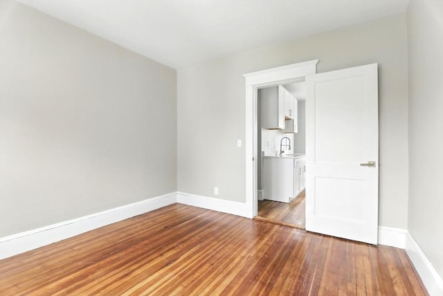 unfurnished bedroom featuring a sink, baseboards, and hardwood / wood-style floors
