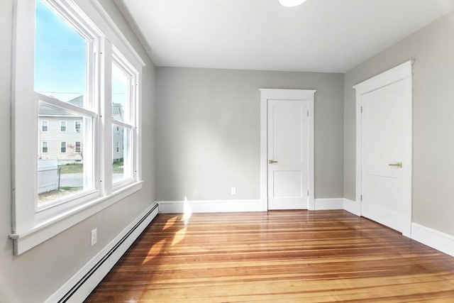 empty room featuring wood finished floors, baseboards, and a baseboard heating unit