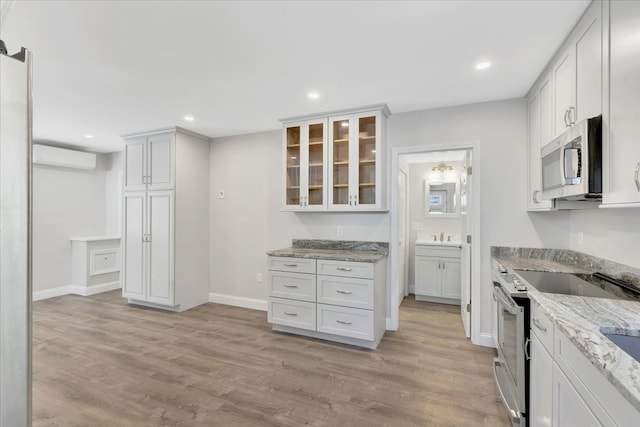 kitchen featuring appliances with stainless steel finishes, white cabinets, light stone counters, and light wood-type flooring