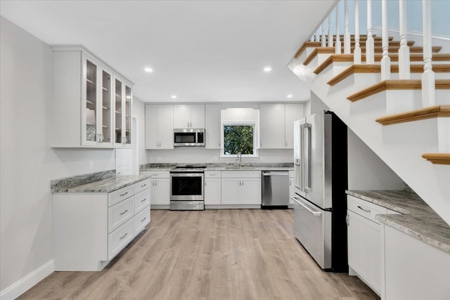 kitchen with appliances with stainless steel finishes, light hardwood / wood-style flooring, white cabinetry, and light stone counters