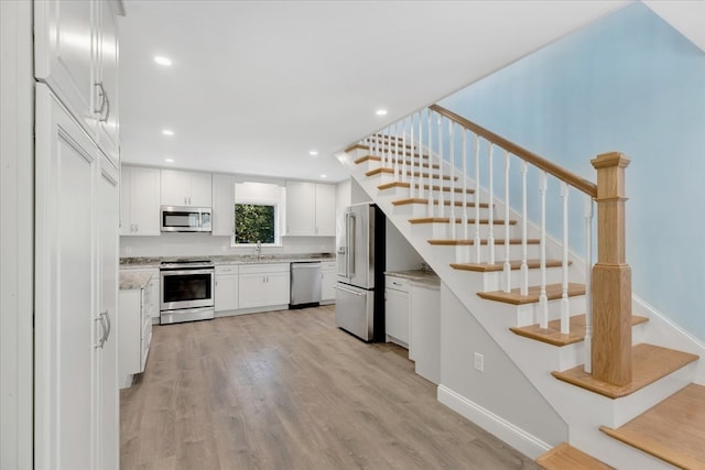 kitchen featuring appliances with stainless steel finishes, light hardwood / wood-style flooring, white cabinetry, and light stone countertops