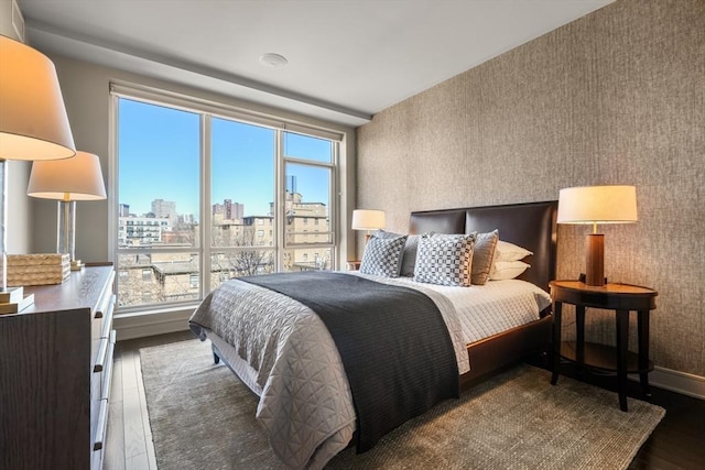 bedroom with baseboards, a view of city, wood finished floors, and wallpapered walls