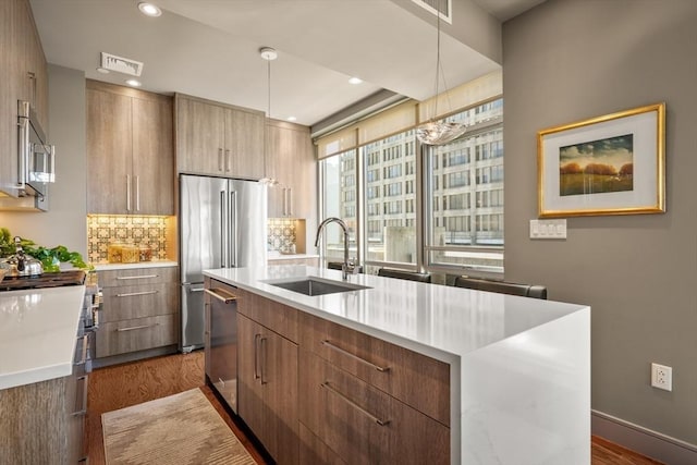 kitchen with a kitchen island with sink, a sink, light countertops, modern cabinets, and premium appliances