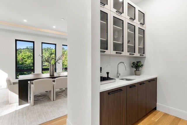 bar featuring baseboards, decorative backsplash, light wood-style floors, a sink, and recessed lighting